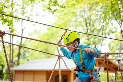 Young boy passing cable route among trees, extreme sport in adventure park Stock Photos