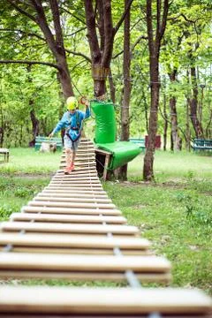 Young boy passing cable route among trees, extreme sport in adventure park Stock Photos