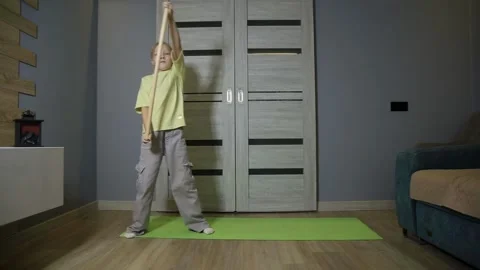 Young boy performs physical exercise with wooden stick indoors. Home fitness Stock-Footage 329622452