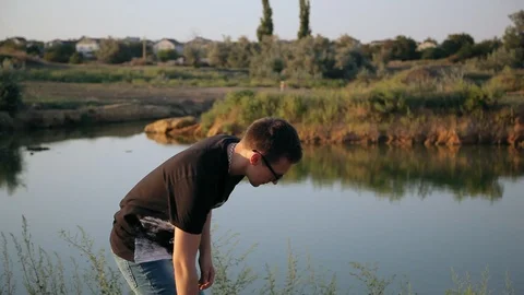 Young boy picks up a stone and throws it into pond 3 Видео 94442365
