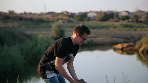 Young boy picks up a stone and throws it into pond 1 Video stock 94442402