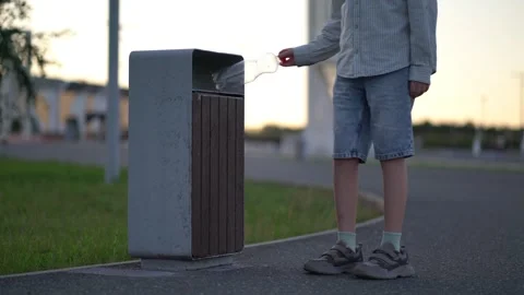 Young boy places plastic bottle into outdoor trash bin at dusk Stock Footage 342084978