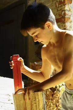 Young boy placing splitting wedge into log during firewood preparation Foto stock