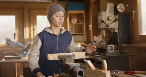 Young boy planes wood in a small woodshed Video stock 85656146