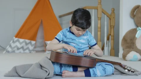 Young boy playing and tuning guitar 4K R3D Video stock 129052460