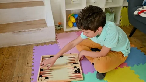 Young boy playing backgammon on colorful floor mats at home Stock Footage 290052893