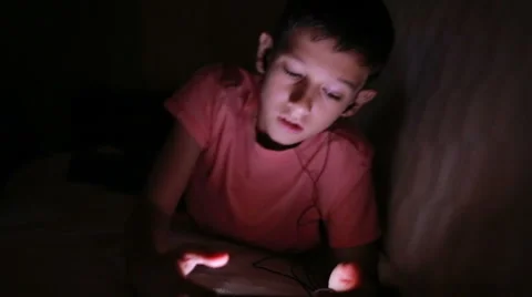 Young boy playing with a cellphone or smartphone on a bed. night Stock Footage