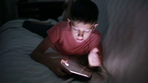 Young boy playing with a cellphone or smartphone on a bed. night Stock Footage 68324695