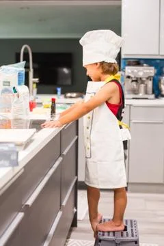 Young boy playing Chef in the kitchen at home wearing apron and hat cooking a Stock Photos