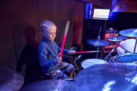 Young boy playing drums in dark studio under blue purple stage light Stockfoto's