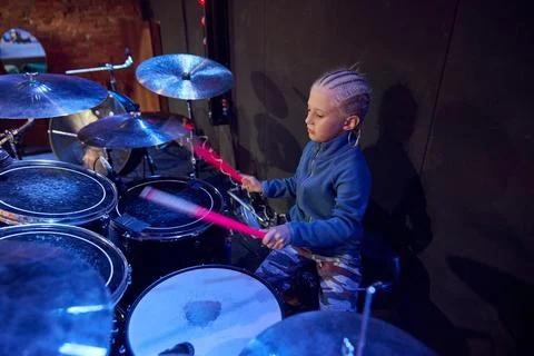 Young boy playing drums onstage under blue and red concert lights Stock Photos