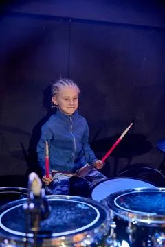 Young boy playing drums on stage under blue concert lighting Stock Photos