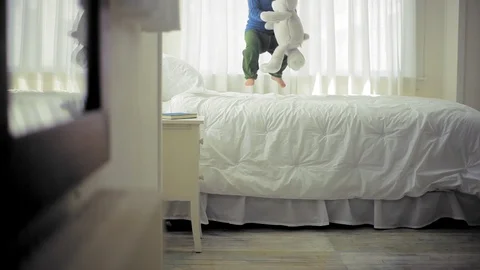 Young boy playing with his teddy bear on his bed in his bedroom. Видео 88341875