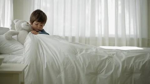 Young boy playing with his teddy bear on his bed in his bedroom. 스톡 동영상 88341883