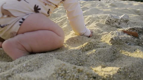Young boy playing joyfully in soft golden sand at the beach, exploring textures Stock Footage 313947781
