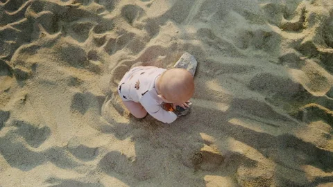 Young boy playing joyfully in soft golden sand on a sunny beach, exploring Stock Footage 314269653