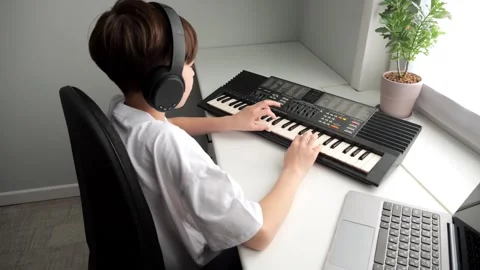 Young boy playing keyboard wearing headphones at home Stock Footage 308439685