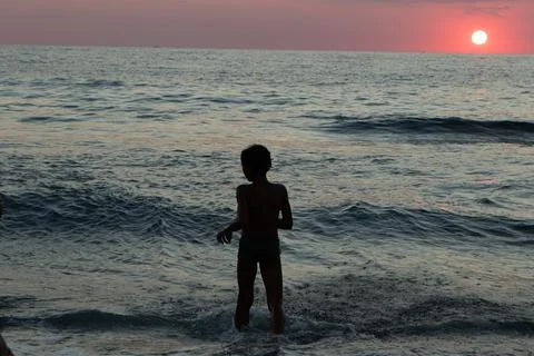 Young boy playing in ocean waves at sunset 스톡 사진