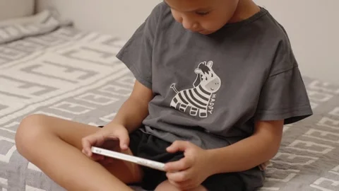 Young boy playing online game sitting on his bed Stock Footage 315508554