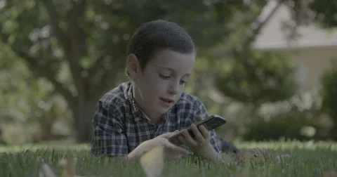 Young boy playing with a smartphone laying on a lawn Stock-Footage 55331111