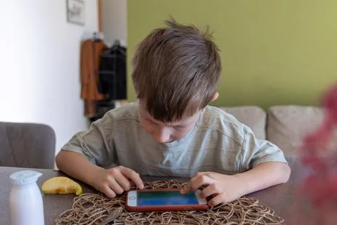 Young boy playing on smartphone at table. A young boy sits at a dining table Stock Photos