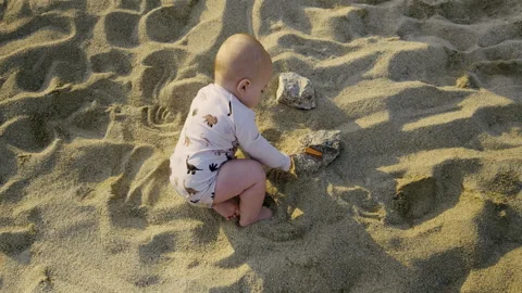 Young boy playing in soft sand on a sunny beach, exploring textures and shapes Stock Footage 313947821