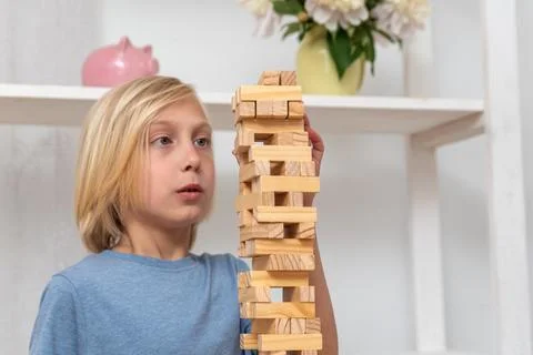 Young boy playing a stacking game, carefully balancing a tall wooden block .. Stock Photos