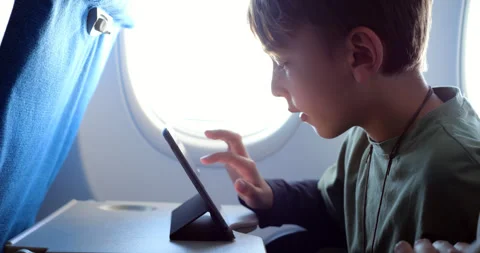 Young boy playing on tablet in flight, move virtual item by finger swipe, slowmo Stock Footage 303993308