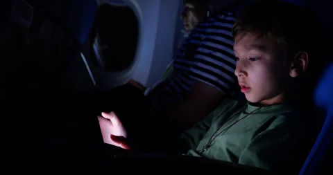 Young boy playing with tablet on night flight, dim economy class cabin Stock Footage 303992611