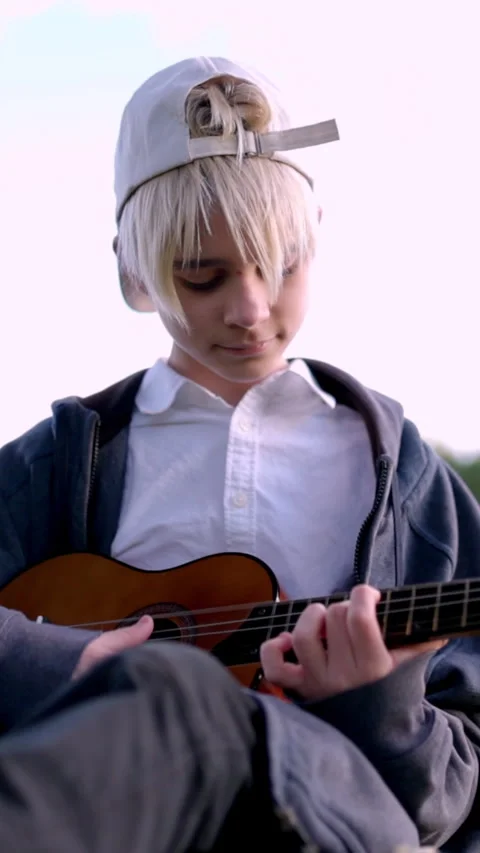 Young boy playing ukulele outdoors in a park Stock Footage 327333389