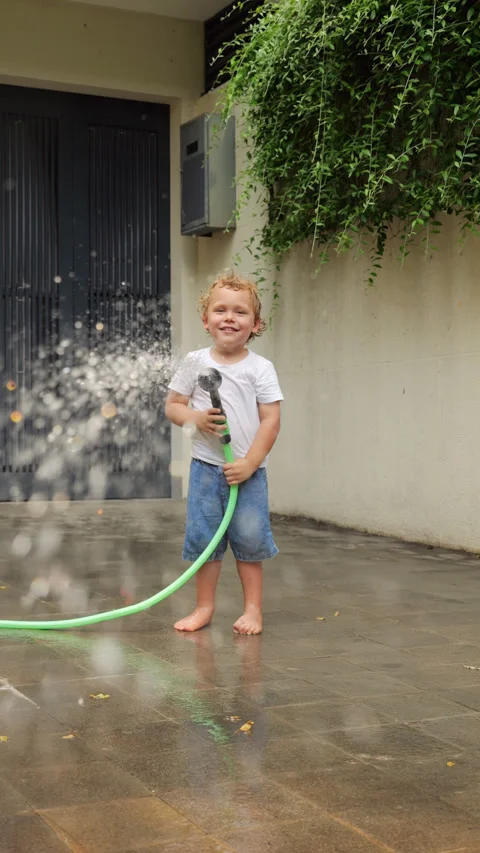 Young boy playing with water, swing sprinkler and directs jet straight to camera 스톡 동영상 310299308