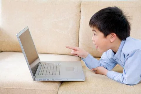 Young boy points at laptop screen on sofa Stock Photos