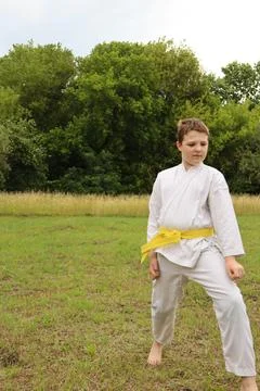 Young boy practices karate in a grassy field during a cloudy day Stock Photos