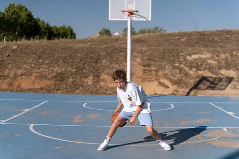 Young boy practicing dribbling while playing basketball on an outdoor court. Foto stock