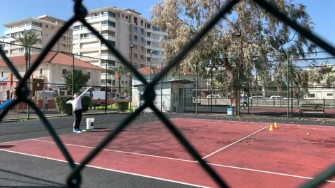 Young boy practicing tennis serving shot through the metal fence Stock Footage 147869035