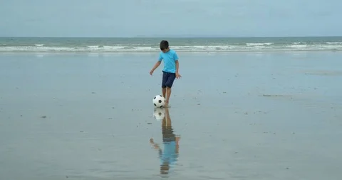 A young boy practising his soccer skills on a beach. Video stock 79794378