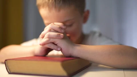 Young boy is praying. A boy prays for a lifestyle child religion. Religious book Stock Footage 320842459