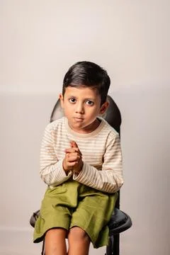 Young Boy Praying with Folded Hands While Sitting on Chair Indoors Stock Photos