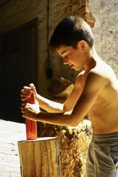 Young boy preparing log with splitting wedge for firewood production outdoors Stock Photos