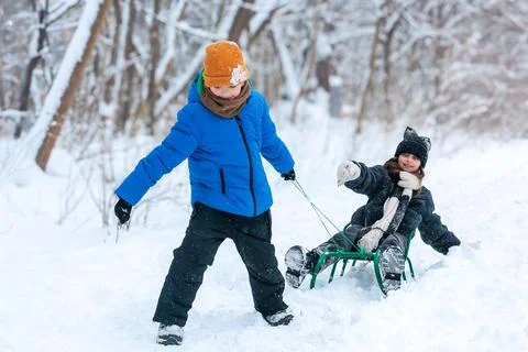 Young boy pulling girl on sled in winter park Stock Photos