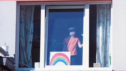 Young boy puts a rainbow paint drawing on window of his house. Home isolation. Stock Footage