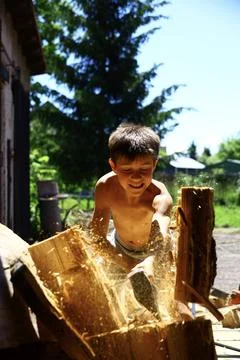 Young boy raising splitting axe high above head while preparing firewood Stock Photos