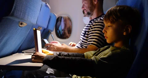 Young boy read from tablet or e-book during night flight, parents near Stock Footage 303992360