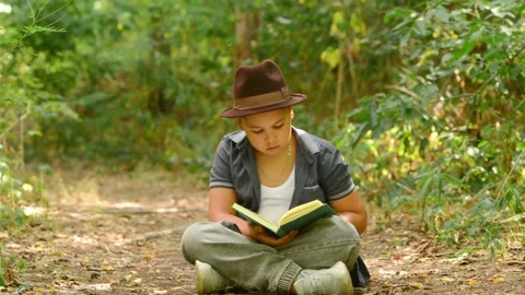 Young Boy Reading Book, Closes It and Dreams Outdoors in Nature Forest Video stock 343550241