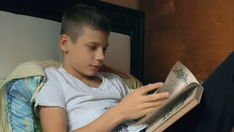 Young boy reading book on sofa. Child reading book. Kid doing homework Stock Footage 69865528