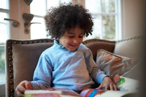 Young Boy Reading Book On Sofa At Home Stock Photos