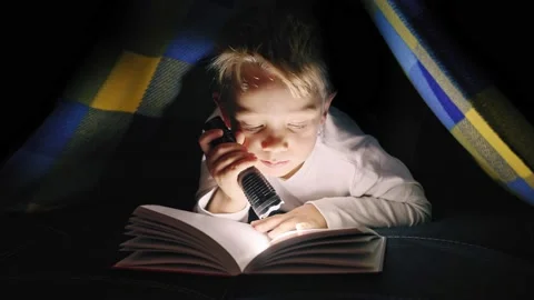Young boy reading a captivating book at night - lighting with a flashlight under Stock Footage 167320697
