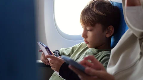 Young boy reading e-book during a flight, mother with phone on foreground Stock Footage 303993207