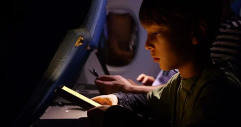 Young boy reading electronic book in airliner, family with gadgets on background Stock Footage 303992013