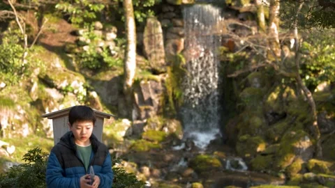 Young Boy Reading Map Near Waterfall in Traditional Japanese Garden Stock Footage 335850771